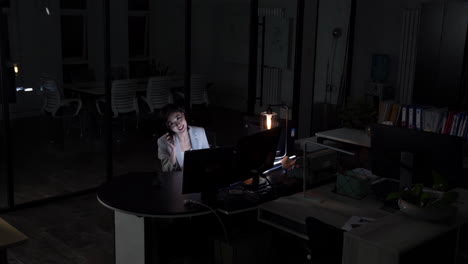 confident businesswoman company manager is talking on mobile phone, using laptop sitting desk working overtime late night. business negotiations, consultation and effective work in modern environment
