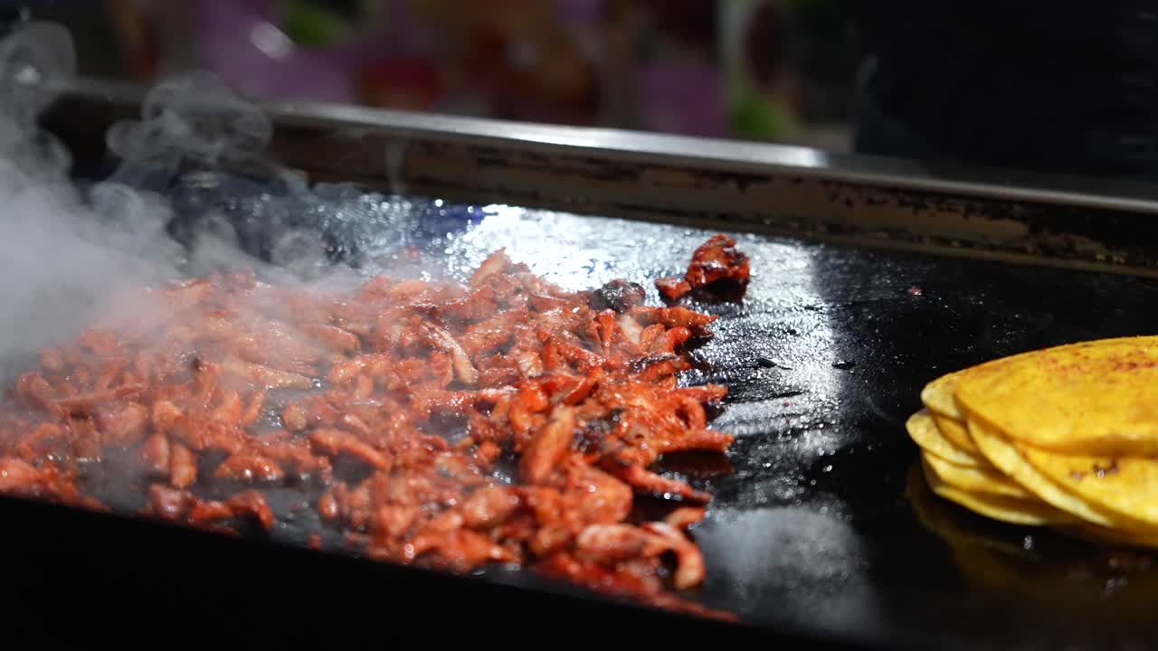 La carne al pastor sfrigolante cuoce su una griglia al rallentatore. Il vapore si alza, sprigionando aromi e sapori intensi, catturando l'esperienza dello street food dei tacos messicani cotti all'aperto.