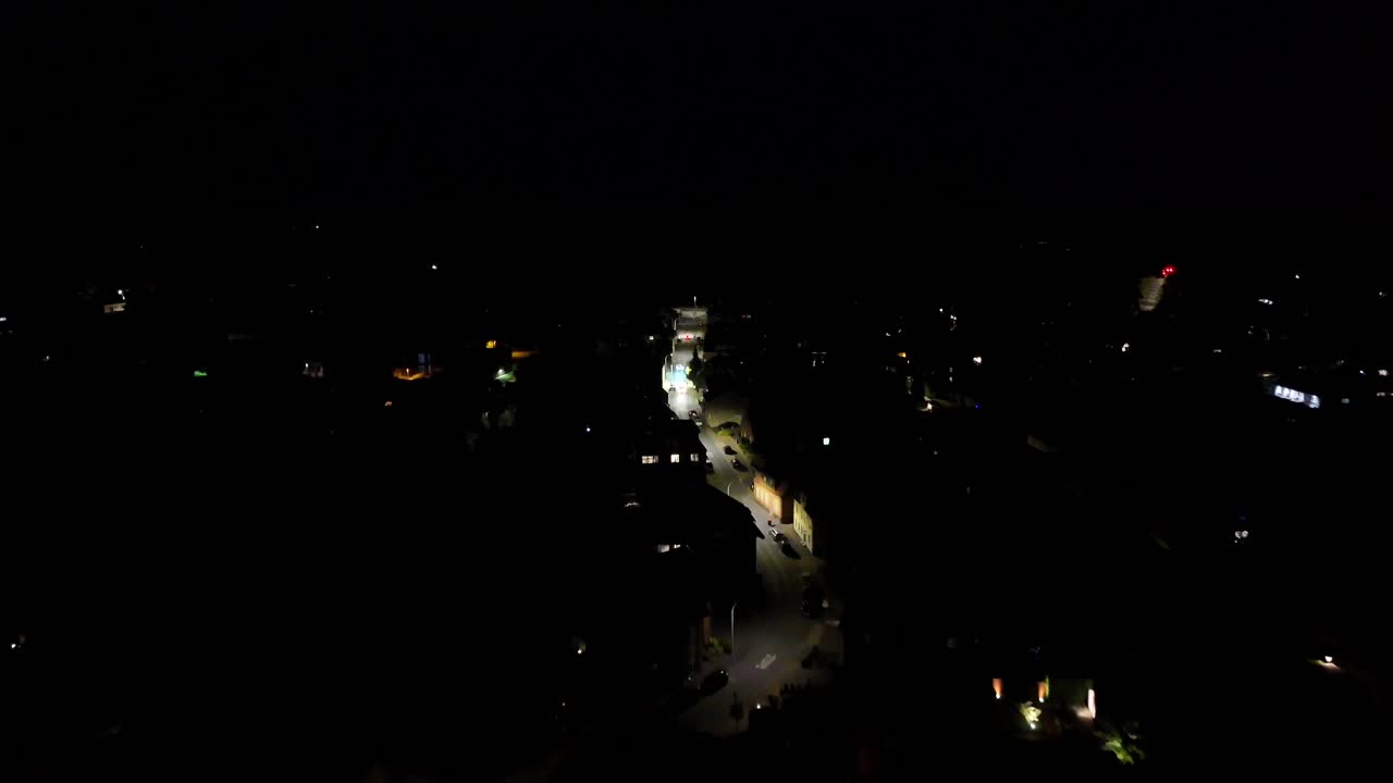 Illuminated street at night in small American town. Lighting lantern along curvy road. Parking cars. Suburb neighborhood homes at midnight. Aerial flyover shot