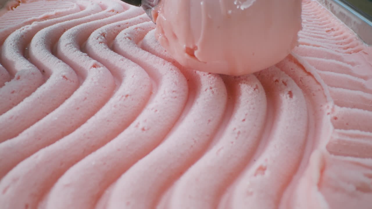 A close-up of a pink lemonade or strawberry ice cream being scooped out with a scoop. Smooth texture, vibrant color, and refreshing appearance.