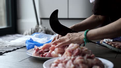 Aruvamanai,-a-traditional-vegetable-cutter,-is-utilized-to-slice-raw-chicken-meat,-demonstrating-the-artistry-of-meal-preparation-and-culinary-skills-in-cooking