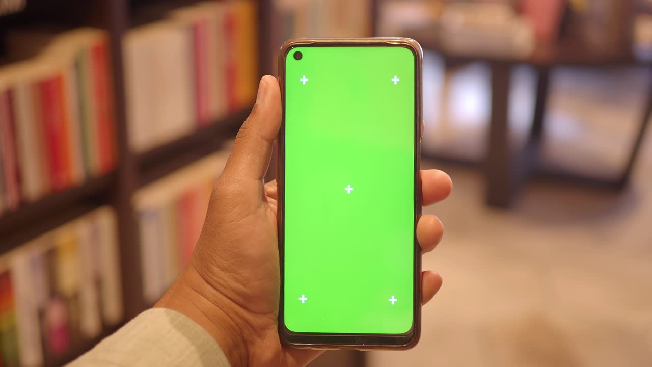 Mano che tiene uno smartphone con schermo verde in una libreria