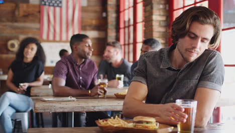 man watching game on screen in sports bar eating burger and fries and drinking beer