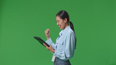 vista lateral de una feliz mujer de negocios asiática celebrando usando una tableta en la pantalla verde en el estudio