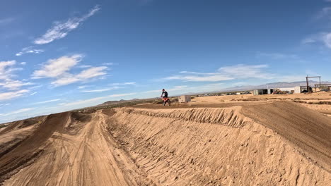 following a motorcycle racing around an off-road track and over a big jump - first person view drone