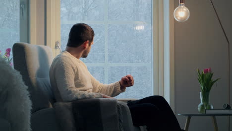 man in sweater looking frustrated and angry in a cozy room with tulips and snow outside, side view, natural light