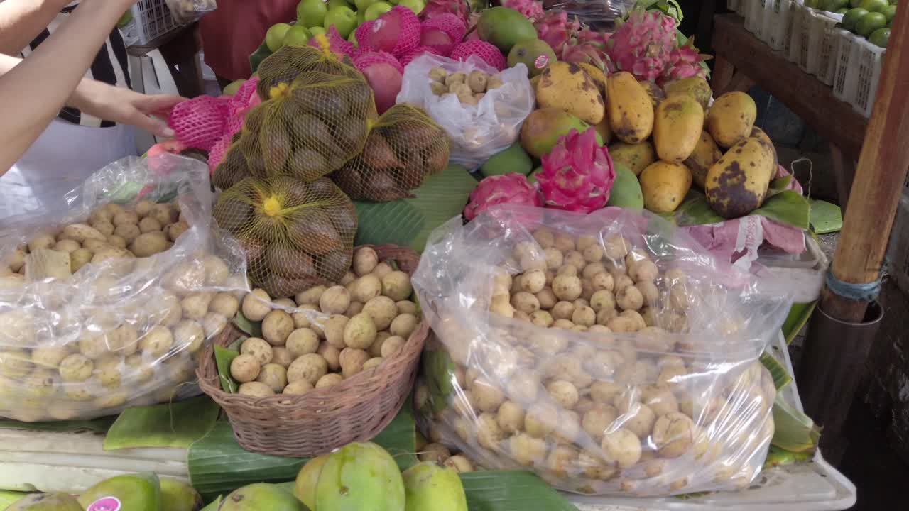 una señora asiática compra una variedad de frutas tropicales langsat, duku, salak, mango, manzana, frutas de dragón naranja en el mercado de frutas tradicionales húmedas asiáticas en indonesia