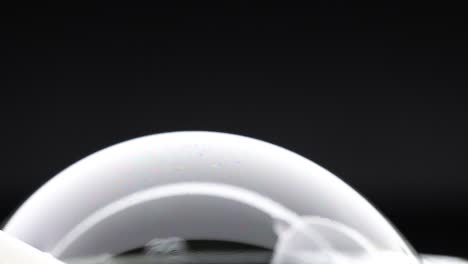 a soap bubble displays evolving colorful reflections against a dark background, showcasing dynamic light and color interplay