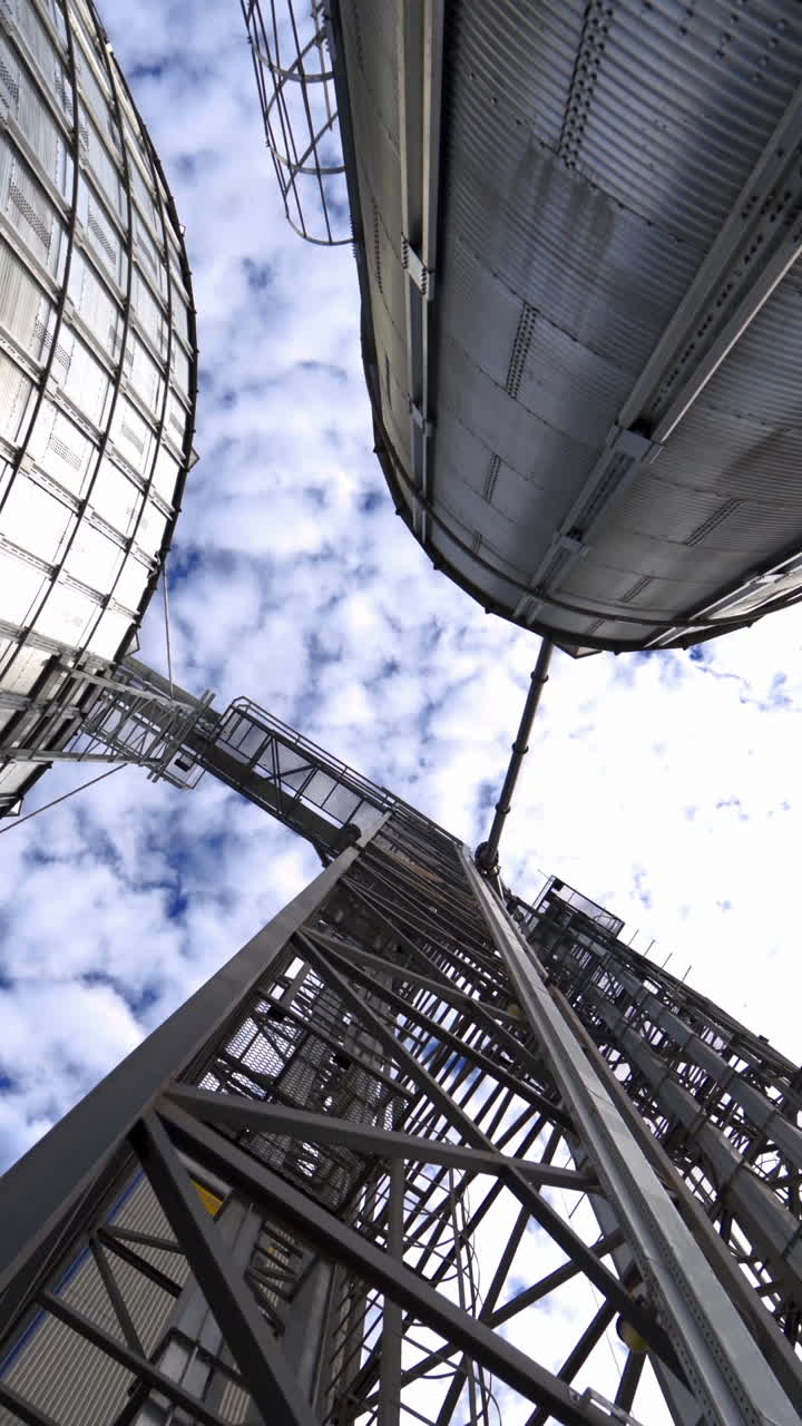 Large industrial plant with storage tanks. Silver grain elevators for agribusiness. Modern warehouse. View from below. Camera circling. Vertical video