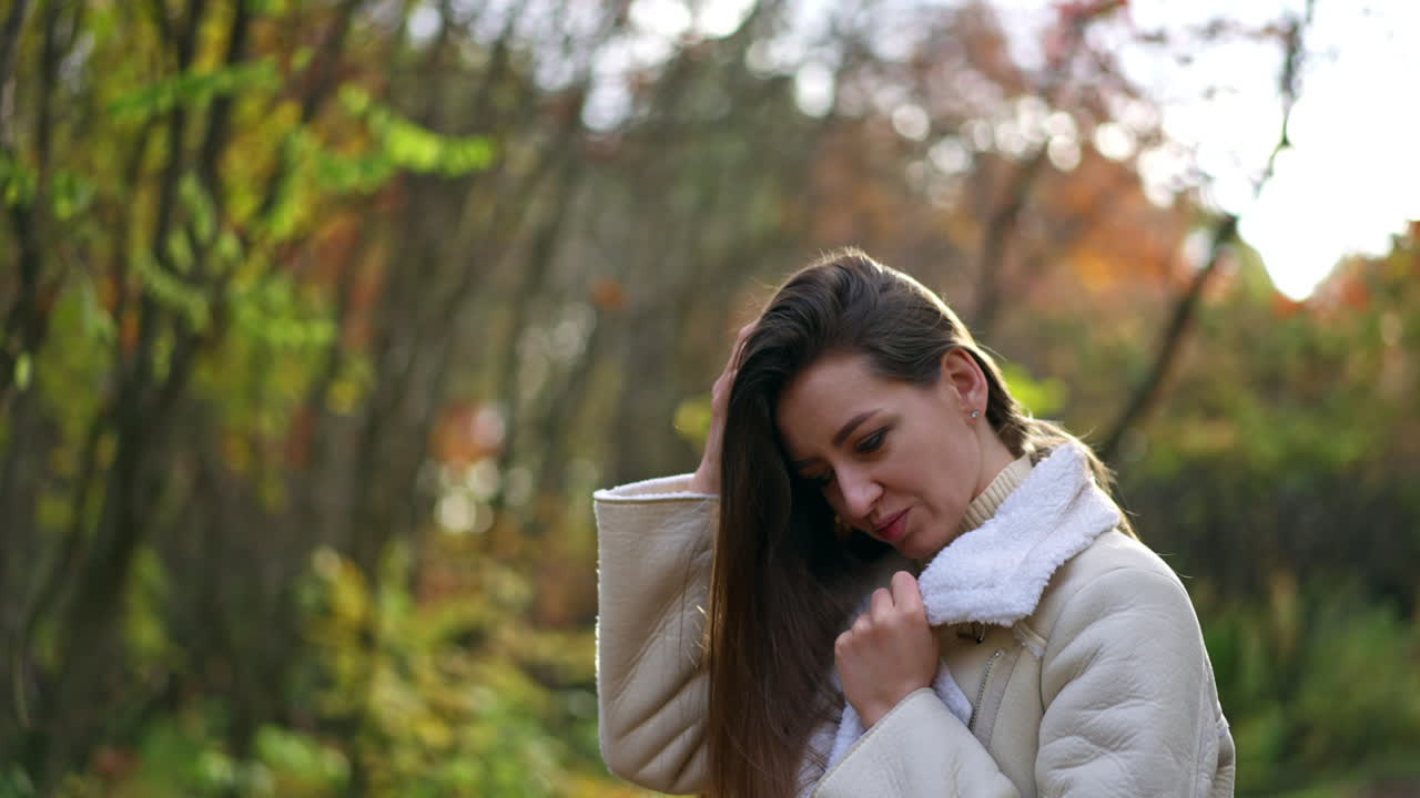 Beautiful Caucasian lady in white jacket turning in front of camera and waving her long hair. A walk by the autumn park on sunny day.