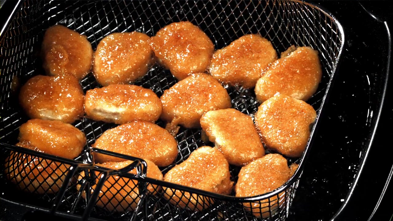 Nuggets de pollo friéndose en aceite caliente en una freidora.