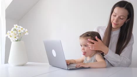 young woman with little daughter at computer in room with modern white wall background young woman with little daughter at computer in room with modern white wall background working mother and little girl