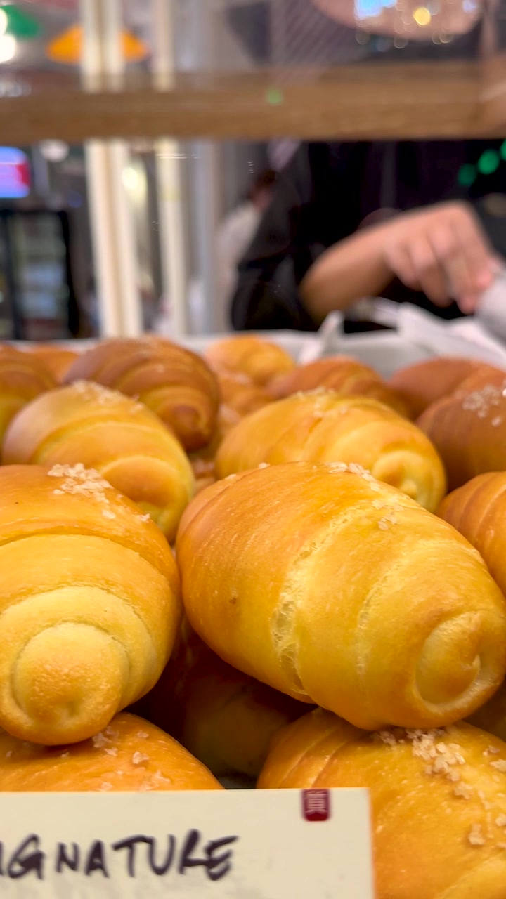 Close-up de pães de sal dourados em exibição com iluminação interna suave e movimento.