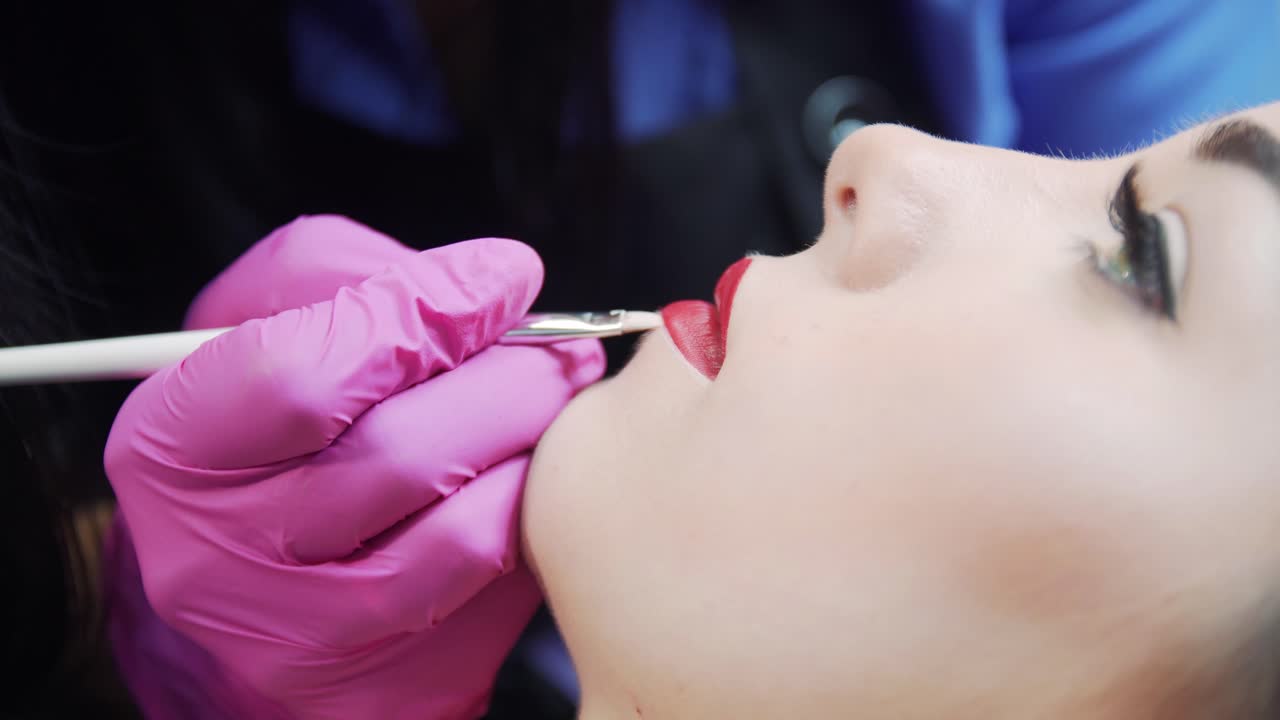 Preparation for the procedure of permanent makeup. Drawing a lip contour with a brush. Girl's face close up