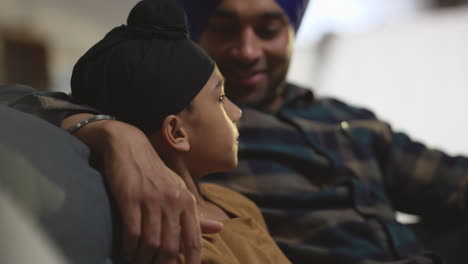 un primer plano de un amante sikh, un padre y un hijo con turbantes, sentados en el sofá de su casa hablando juntos, filmado en tiempo real.