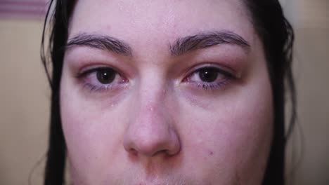 Slow-blinking-woman-in-shower-looks-from-side-to-camera,-Extreme-Close-Up