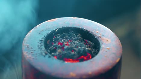 extreme close up of tobacco burning inside a pipe that has been damaged by the fire being always in close distance leaves producing thick clouds of smoke that is blue colour shade and ash is visible