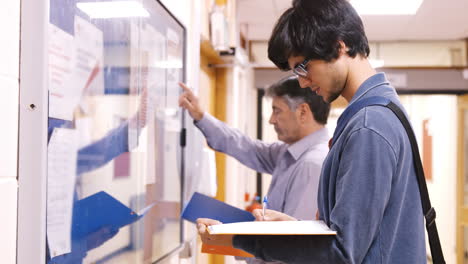estudiante y maestro comprobando papeles colgados en el pasillo