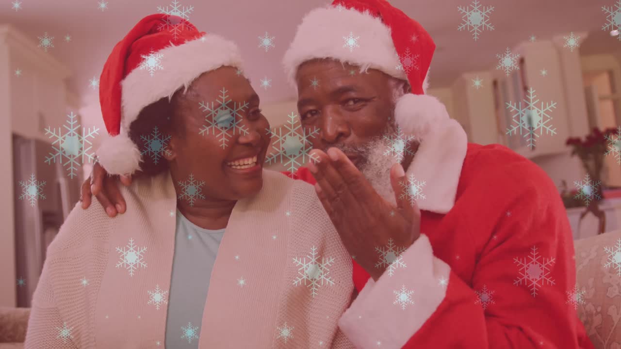 animación de nieve cayendo sobre una pareja sonriente con sombreros de santa y agitando las manos