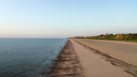 Drohnenluftaufnahme,-Die-Bei-Sonnenaufgang-An-Einem-Langen,-Leeren-Sandstrand-An-Der-Küste-Von-Norfolk-Mit-Sehr-Ruhigem-Wasser-Und-Ohne-Menschen-Fliegt