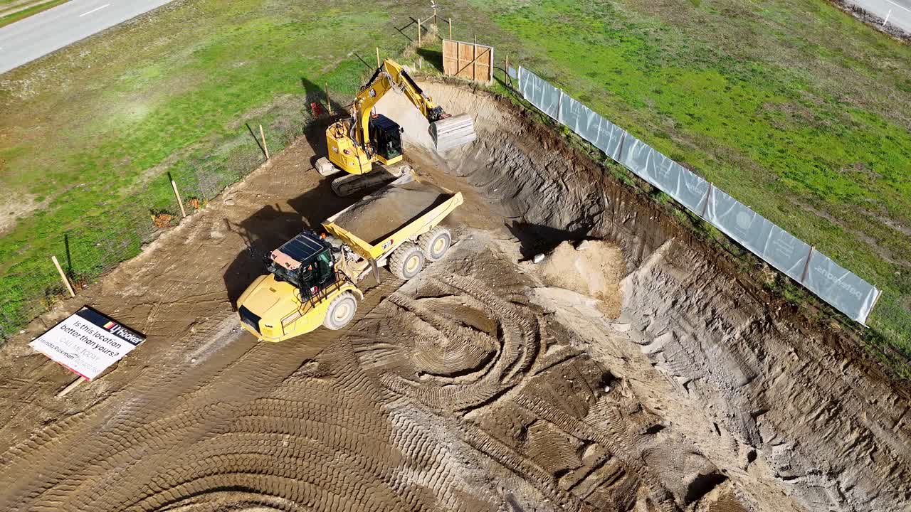 Excavator and dump truck operate on a sunny day, moving earth at a construction site in Cromwell, New Zealand