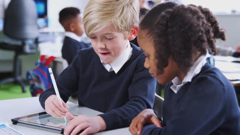 schoolboy using a tablet and stylus with a girl at a desk in a primary school class, close up