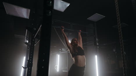 a sporty young woman pulls herself up on a horizontal bar in a dark gym in a beautiful neon backlight. endurance and perseverance in pulling up movement towards the goal