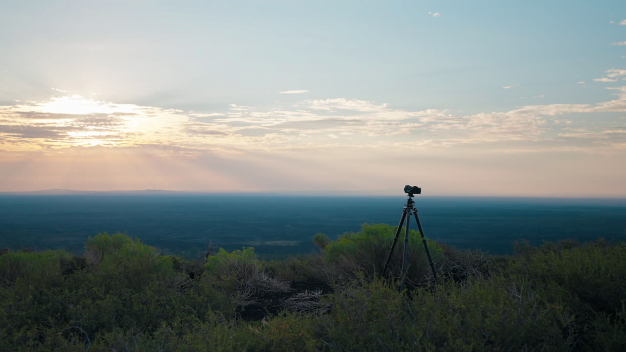 Camera on a tripod capturing a sunset over a vast landscape