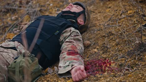 A-soldier-in-camouflage-uniform-and-black-body-armor-seriously-wounded-in-the-arm-is-rendered-unconscious-in-the-steppe-during-military-operations.-A-wounded-soldier-lies-and-waits-for-help-to-provide-first-aid-and-stop-blood-loss