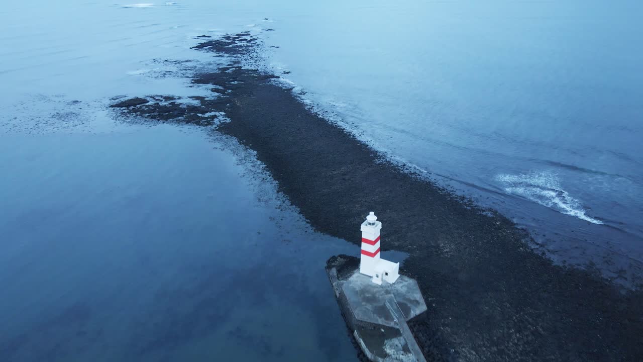 avión no tripulado volando sobre un hermoso antiguo faro en islandia y volando sobre una playa negra hacia un océano tranquilo