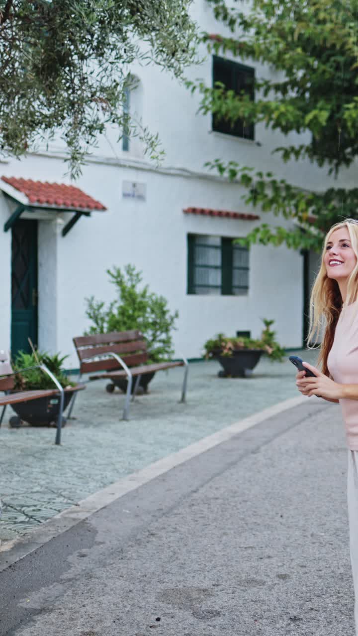 Felice giovane donna che cammina e scatta foto con lo smartphone in città.