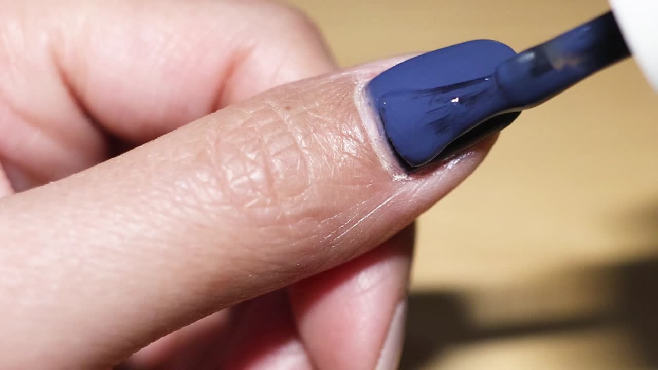 Detailed view of applying blue nail polish on a thumbnail using a brush.