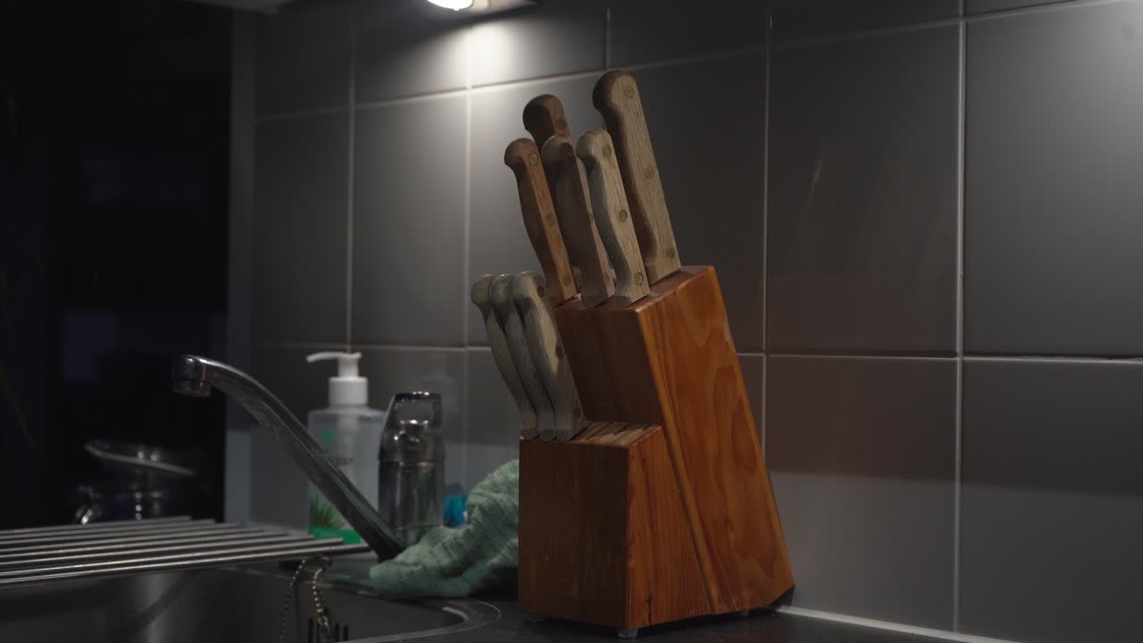 la mano caucásica en la cocina de azulejos saca un cuchillo del bloque de cuchillos de madera
