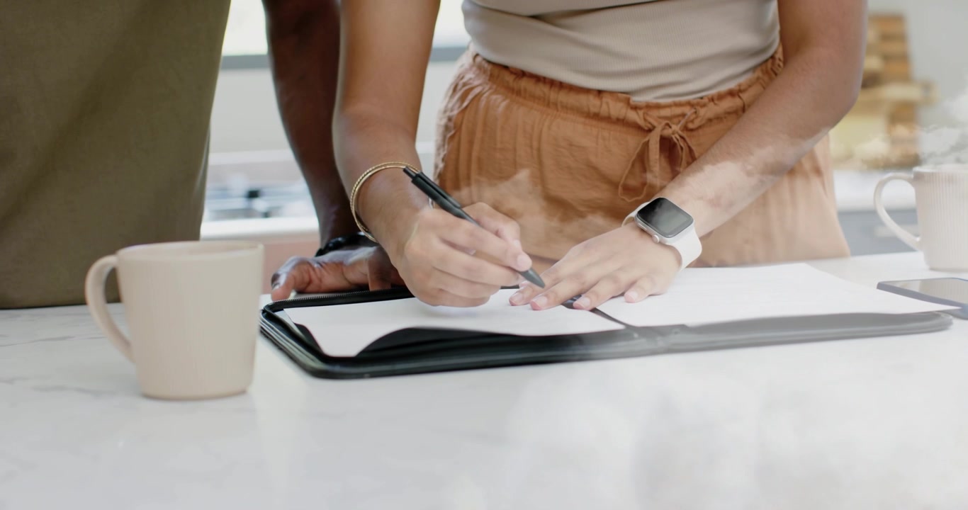 Woman opening portfolio, lifting sheets, picking pen, signing finance forms on kitchen counter
