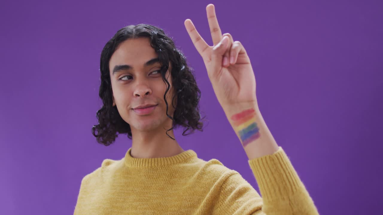 retrato de un hombre biracial feliz con bandera lgbt en el brazo sobre un fondo púrpura