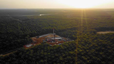 Cinematic-4K-Drone-Footage-of-Onshore-Drilling-Rig-equipment-structure-for-oil-exploration-and-exploitation-in-the-middle-of-jungle-surrounded-by-palm-oil-trees-during-sunset-and-high-oil-price