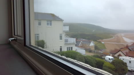 rain flowing down a window with a beach visible in the background in slow motion