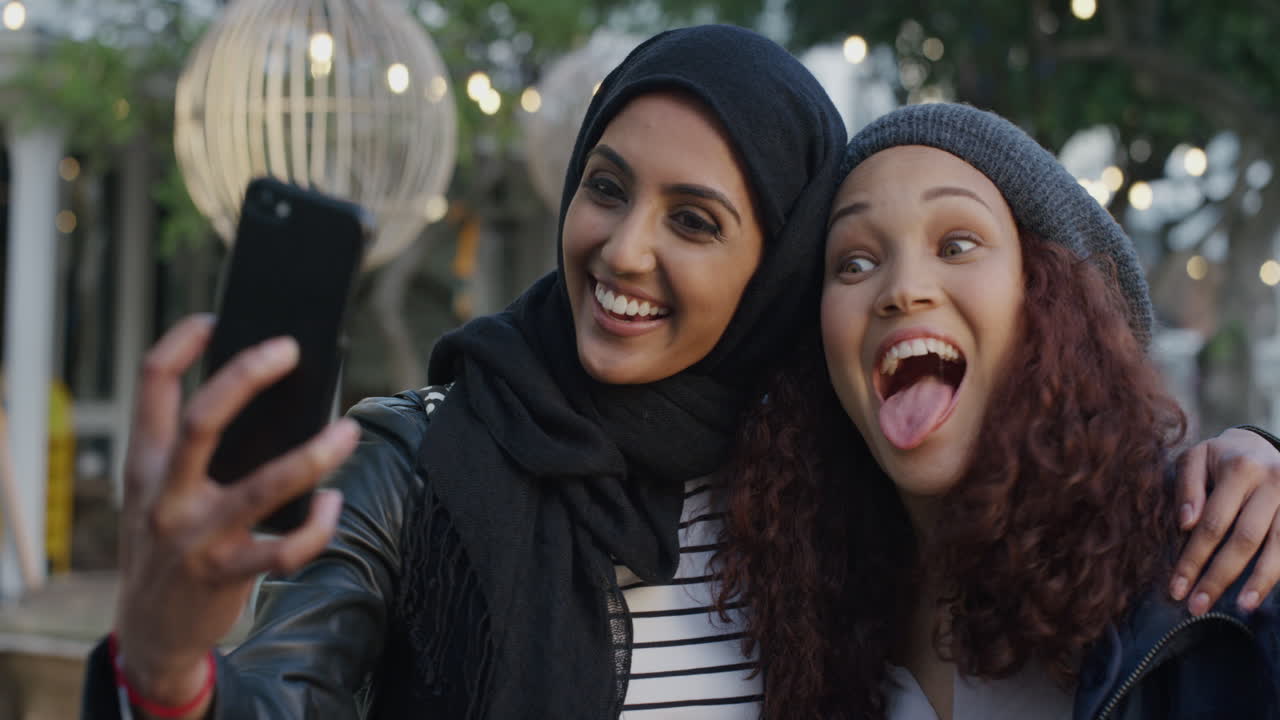 retrato de mujeres jóvenes diversas amigas usando teléfonos inteligentes tomando fotos de selfie haciendo caras disfrutando de diversión relajada amigas pasar el rato en la ciudad en cámara lenta