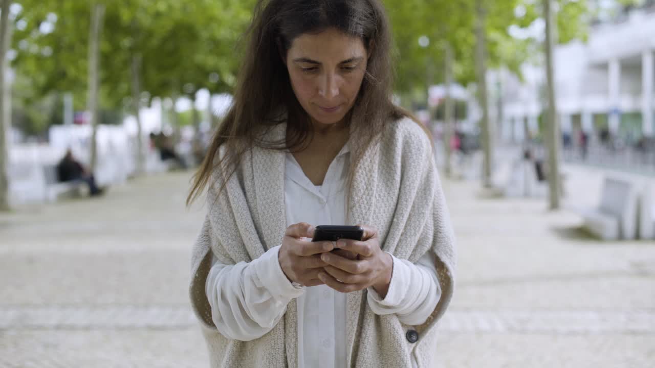 mujer de mediana edad sonriente usando un teléfono inteligente al aire libre.