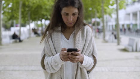 Mujer-Sonriente-De-Mediana-Edad-Usando-Un-Teléfono-Inteligente-Al-Aire-Libre.