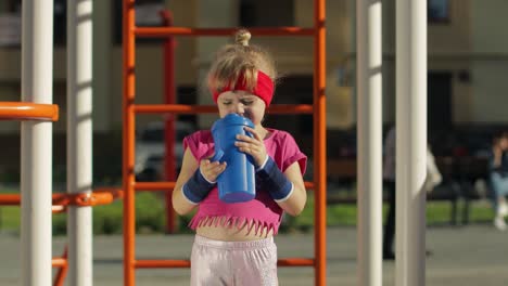 niña con ropa deportiva bebiendo agua para refrescarse después de los ejercicios de fitness. niño pequeño atlético