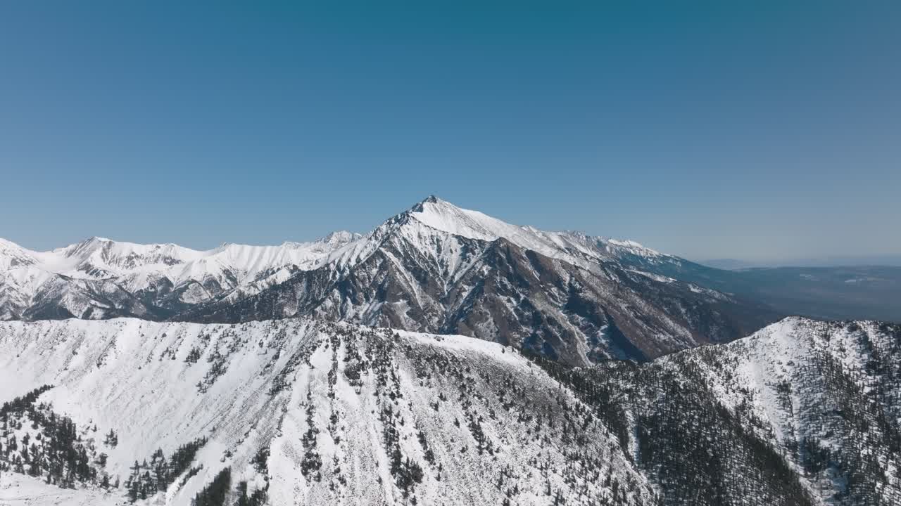 Riprese con drone del Picco Galina e delle creste montuose innevate vicino al villaggio di Arshan, Repubblica di Buriazia, Russia, sotto un cielo azzurro e limpido in una giornata di sole.