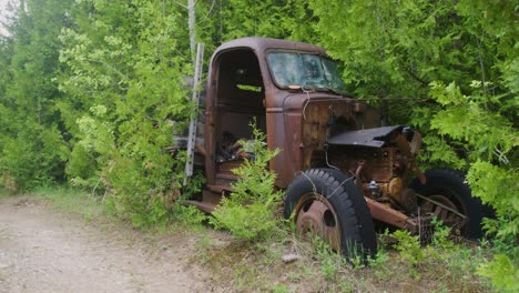 Toma-Panorámica-Que-Muestra-La-Carretera-Desierta-Y-Luego-Un-Camión-Abandonado-De-Los-Años-40-Oxidándose-Y-Cubierto-De-Maleza-Y-árboles.