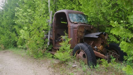 una toma panorámica que muestra la carretera desierta y luego un camión abandonado de los años cuarenta oxidándose y cubierto de malezas y árboles.