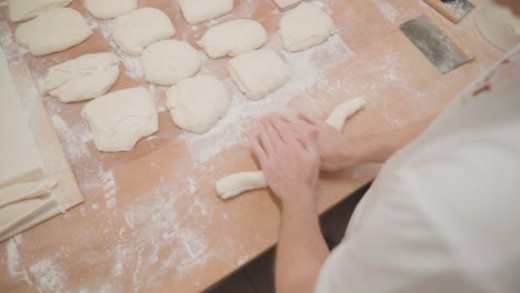 baker rolling fresh dough for baguette, over shoulder slow motion