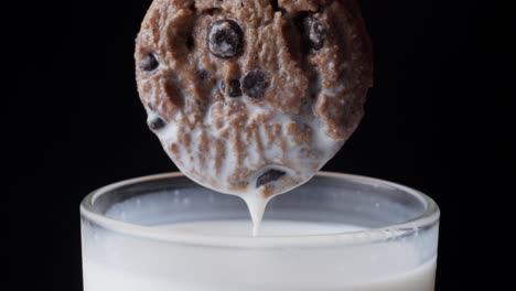 un primer plano con la mano sumergiendo galletas de chocolate en un vaso de leche fresca.