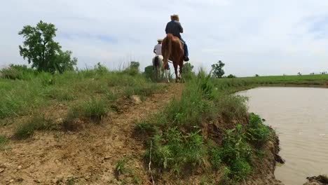 Aerial-close-to-ground-follow-cowboys-are-they-ride-away-from-a-watering-hole,-Kansas