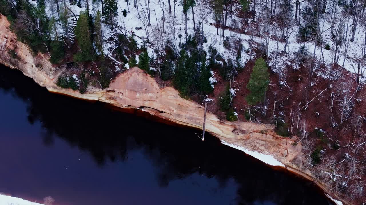 Aerial shot of steep river cliffs and snow-patched forest in Baltic winter light