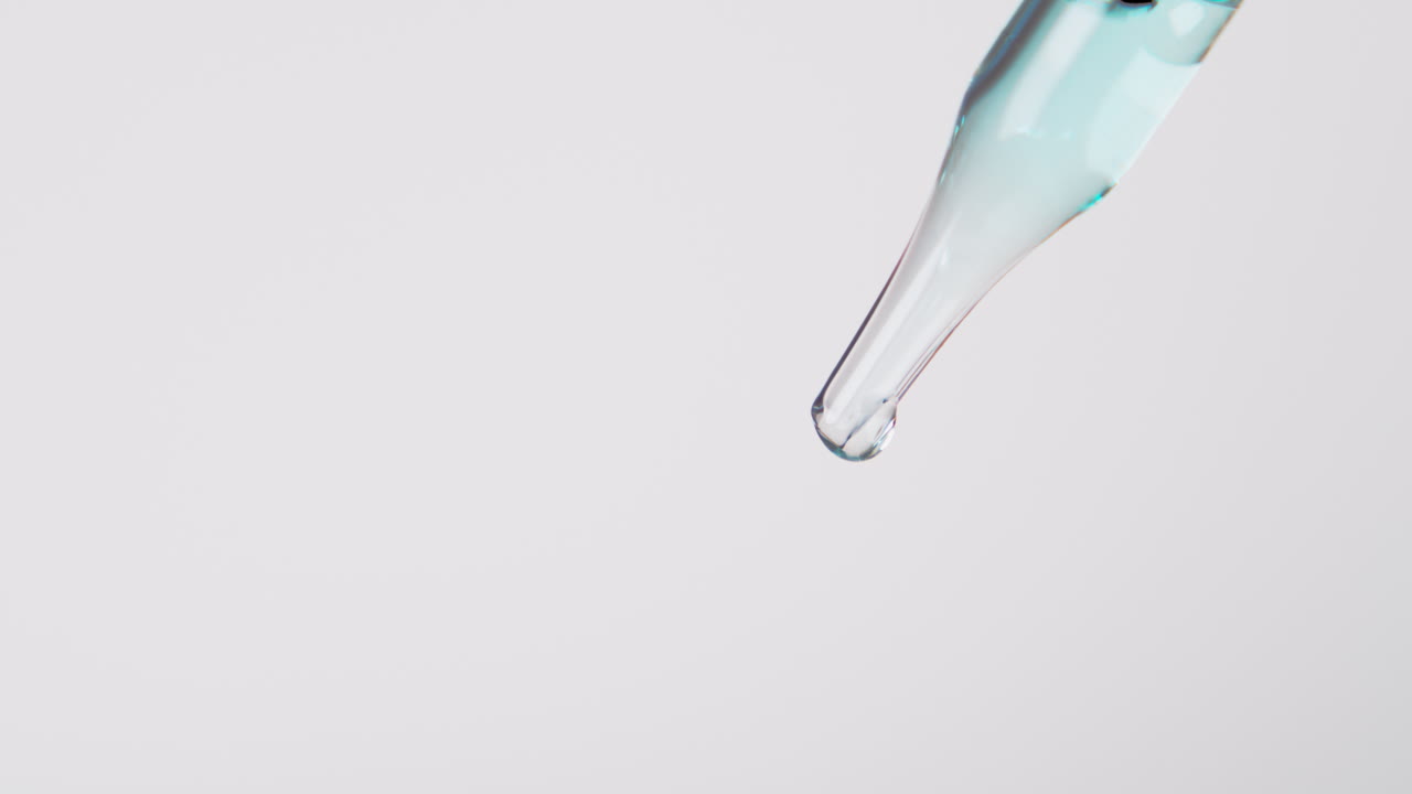 A bluish liquid flowing from a transparent pipette, close shot