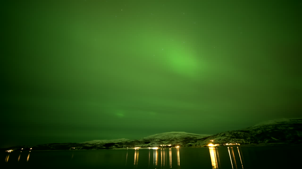 Northern lights (aurora borealis) over the Kongsfjorden fjord with snow covered mountains in view, Timelapse